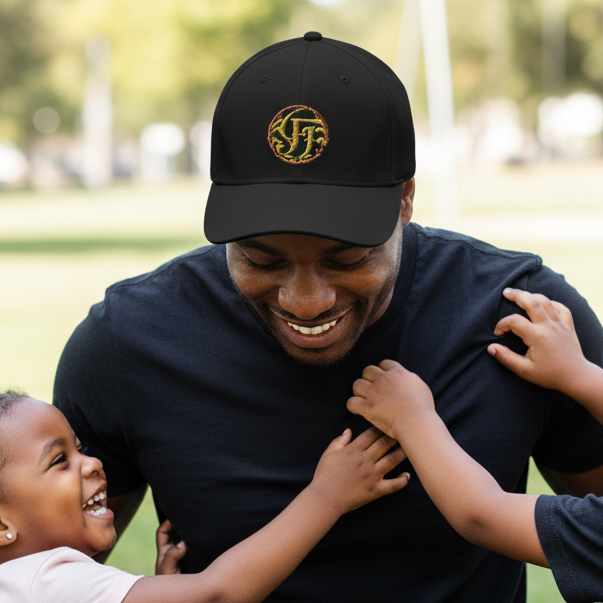Man in a black cap and dark shirt sitting on grass with two children, smiling.