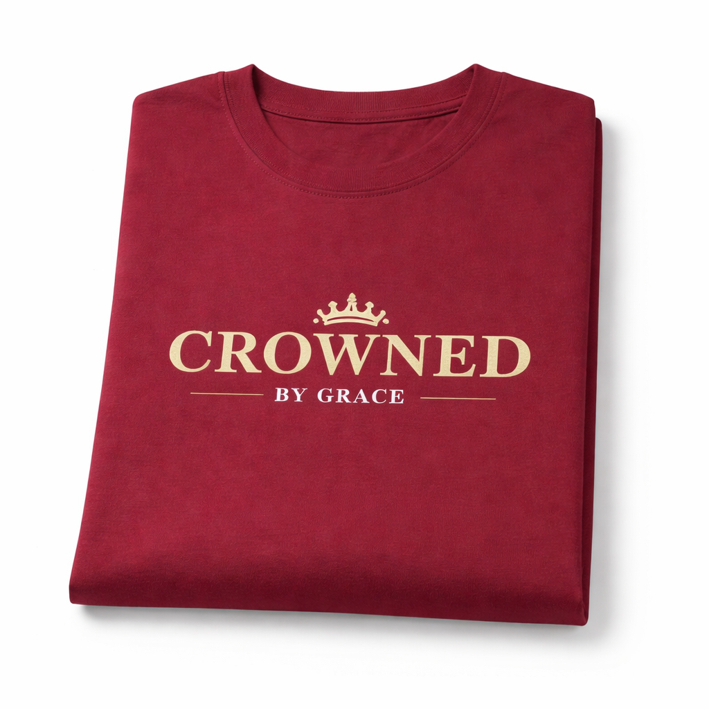 Folded maroon t-shirt with 'Crowned by Grace' text on a white background