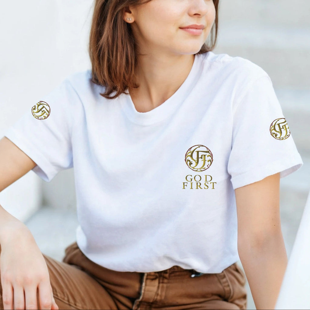 Woman wearing a white t-shirt with gold logos and text, sitting outdoors.