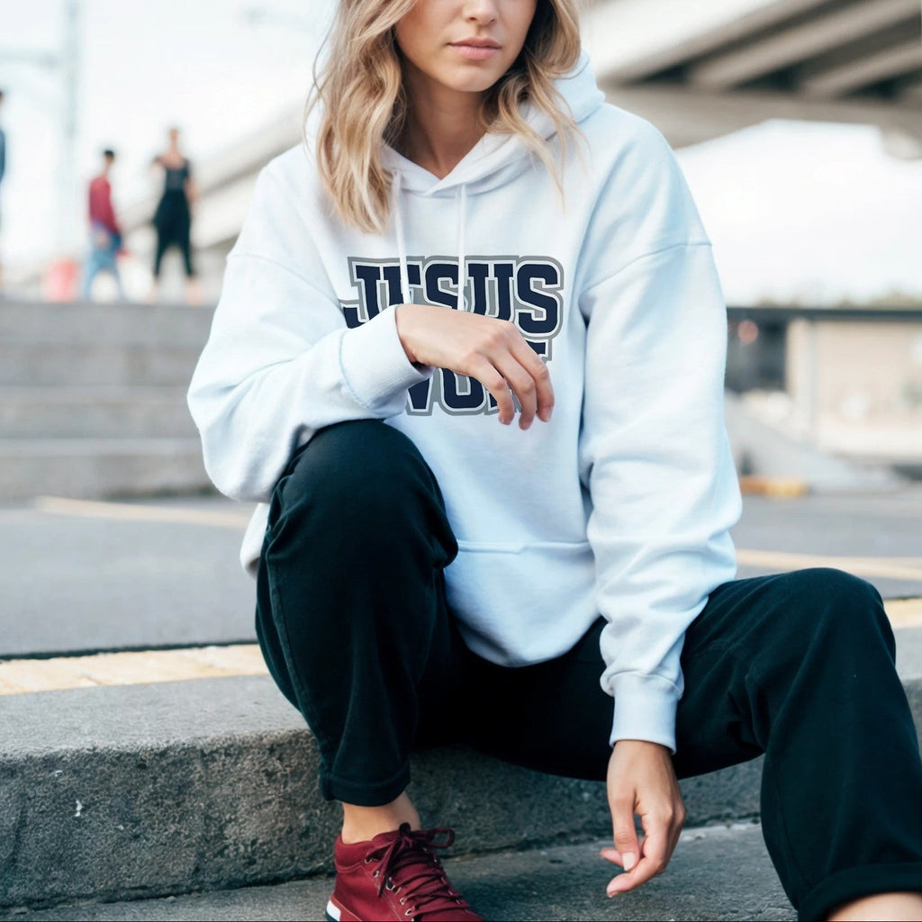Woman wearing a white hoodie with 'JESUS' printed on it, sitting on steps outdoors.
