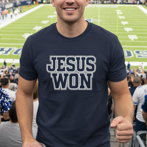 Man wearing a 'Jesus Won' t-shirt at a sports event with a stadium in the background