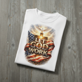 White t-shirt with 'Let God Work' design featuring an American flag on a wooden surface