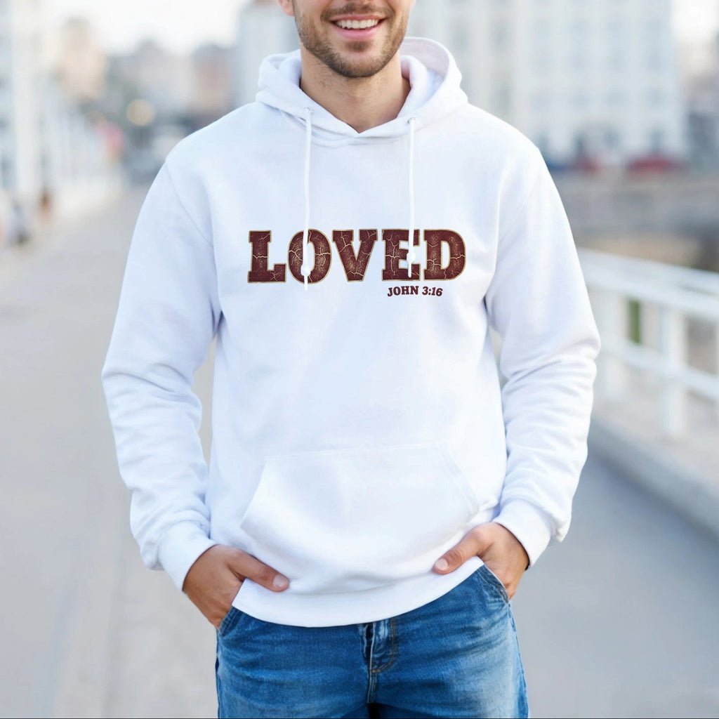 Man wearing a white hoodie with 'LOVED' printed on it, standing outdoors with a blurred cityscape background.