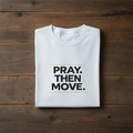 White t-shirt with 'PRAY. THEN MOVE.' text on a wooden surface