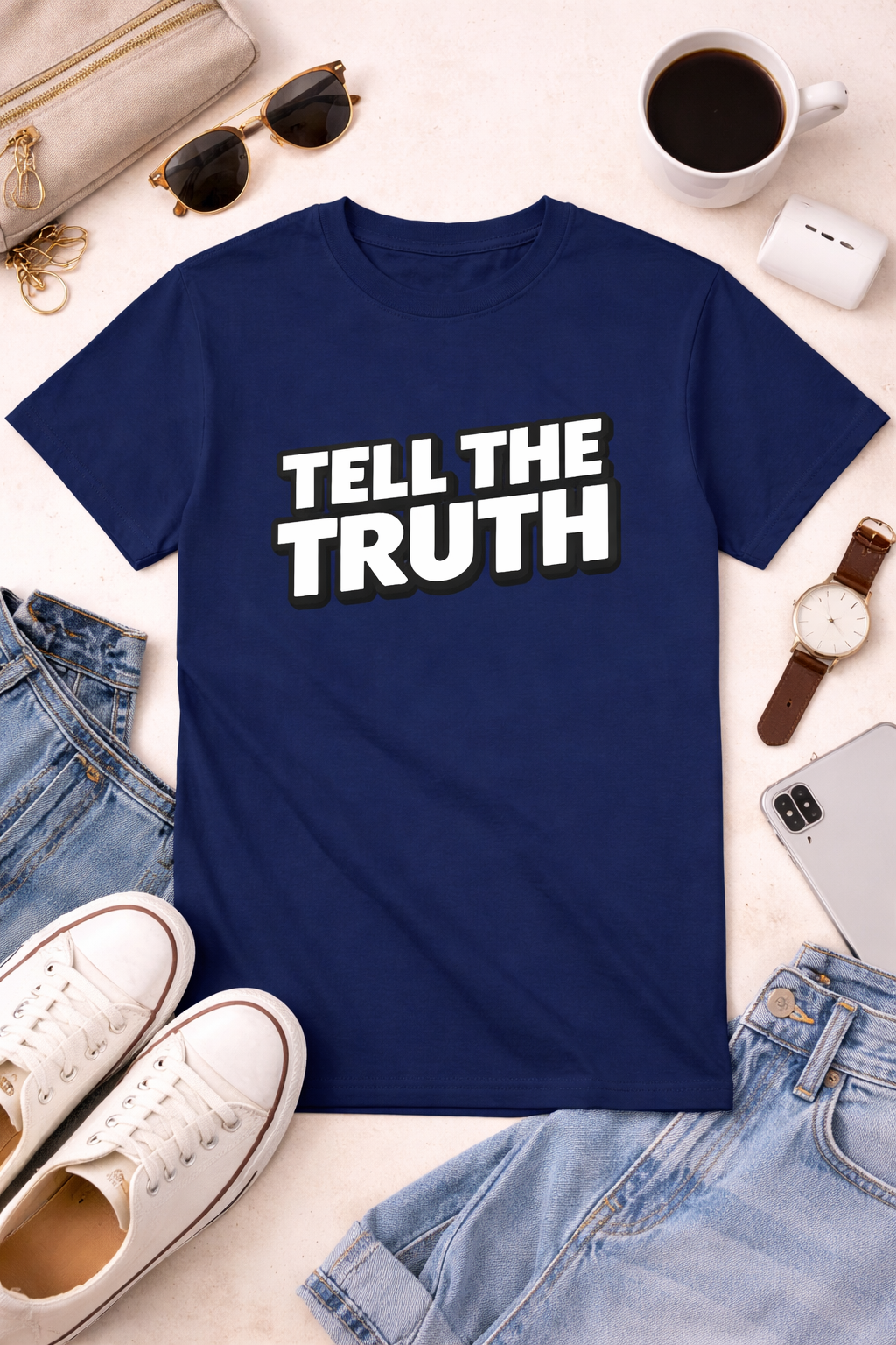Blue t-shirt with 'Tell the Truth' text on a white surface with casual items around