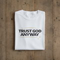 White t-shirt with 'Trust God Anyway' text on a wooden surface