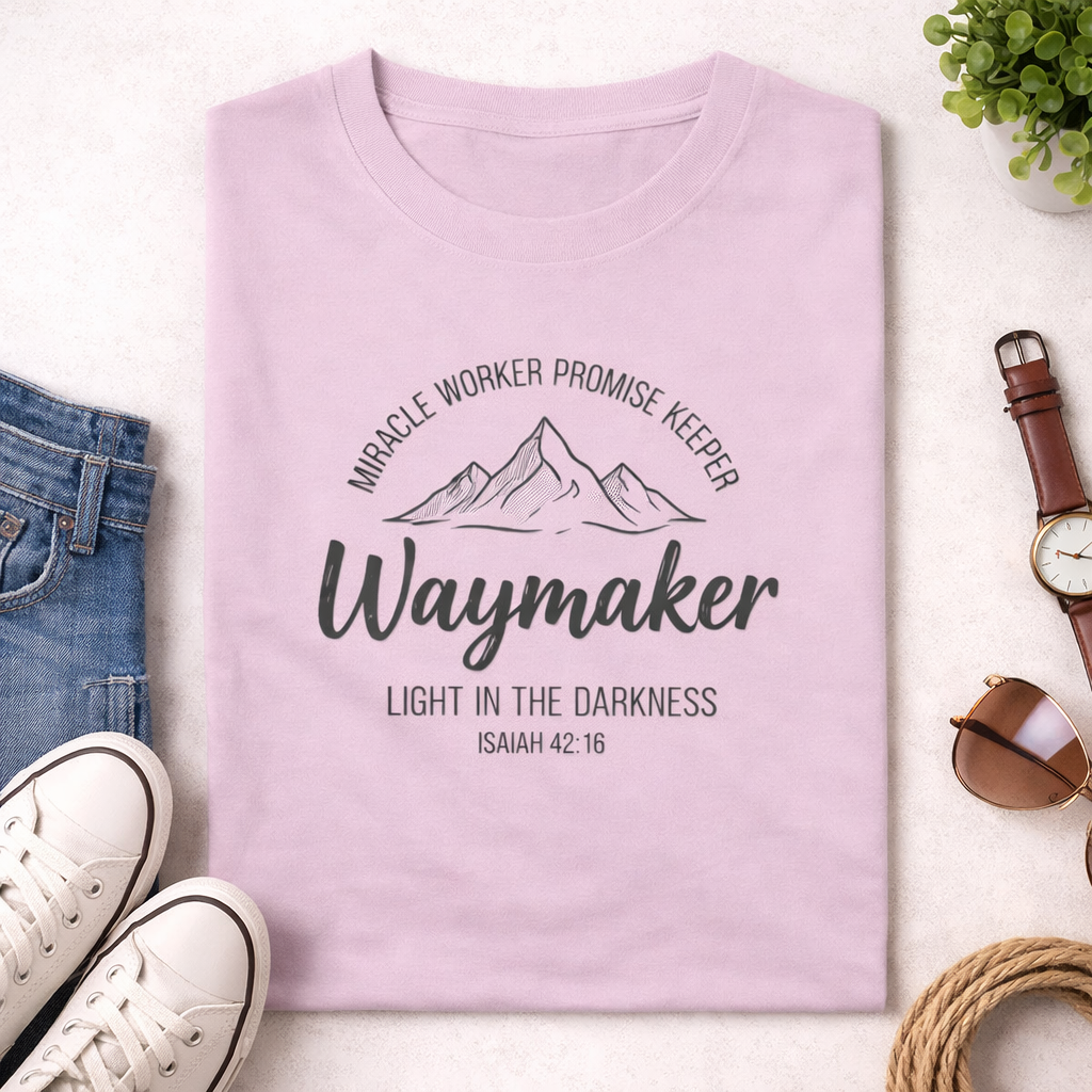 Pink t-shirt with motivational text and mountain graphic on a white surface with accessories.