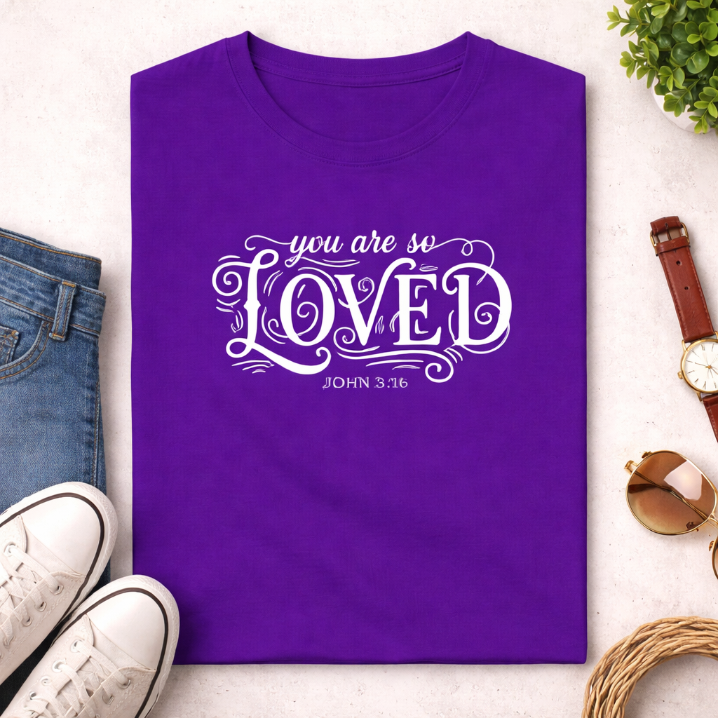 Purple t-shirt with 'you are so loved' text on a light surface with casual items around